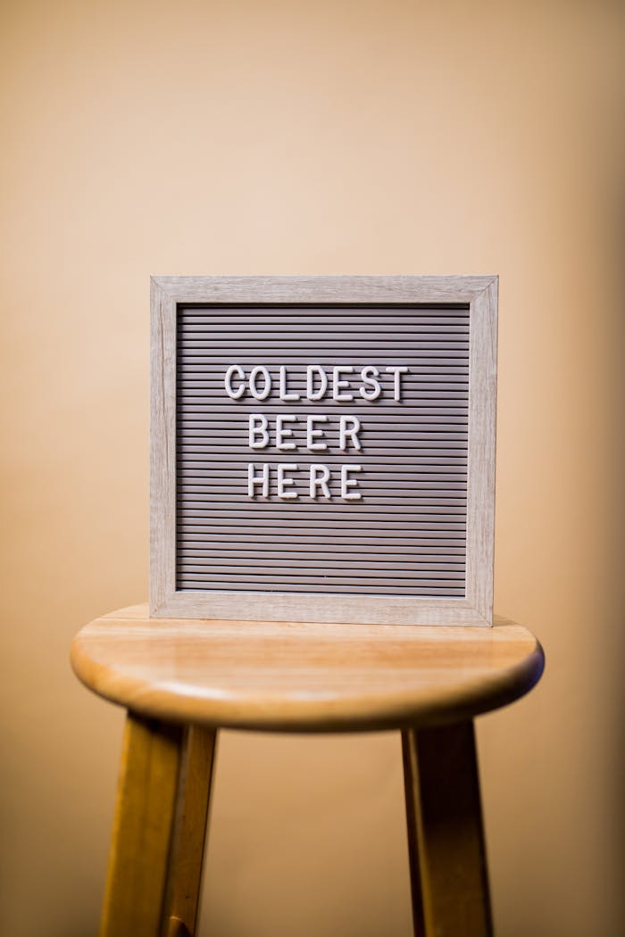 Retro sign displaying 'Coldest Beer Here' on a vintage stool.
